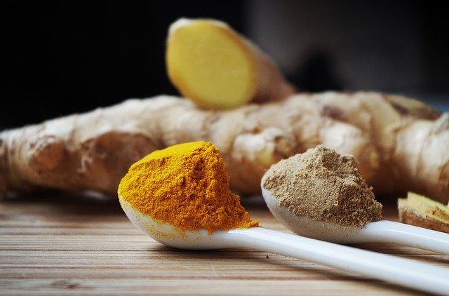 white spoons of colorful turmeric powder, turmeric root in the background